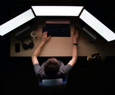 A man working with multiple monitors in a low light room