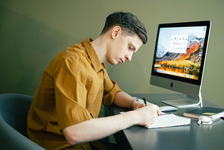 Student in yellow shirt studying on his desk with a notebook and computer