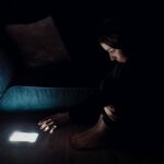 Young woman in black dress trying to stay away with shiny smartphone in the dark